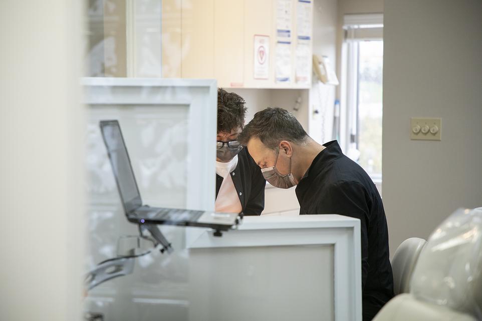 Orthodontist examining patient's teeth using laptop in modern dental office treatment room.