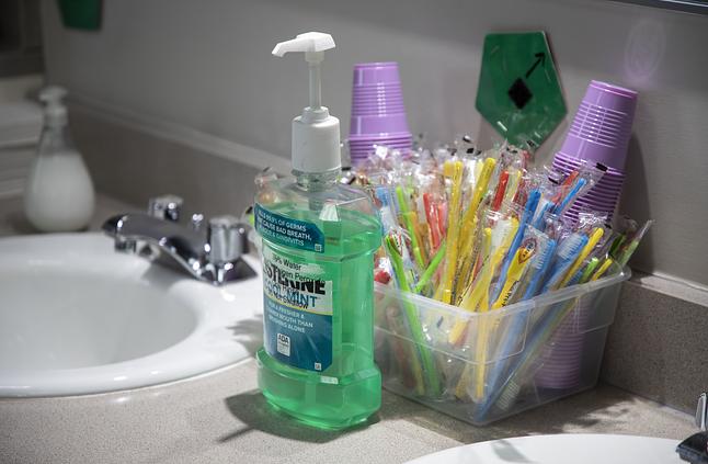 Bathroom sink counter with hand sanitizer, toothbrushes, and toiletries in organized containers.