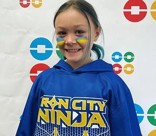Young girl smiling at camera wearing blue "Rancity Ninja" hoodie at orthodontics office event.