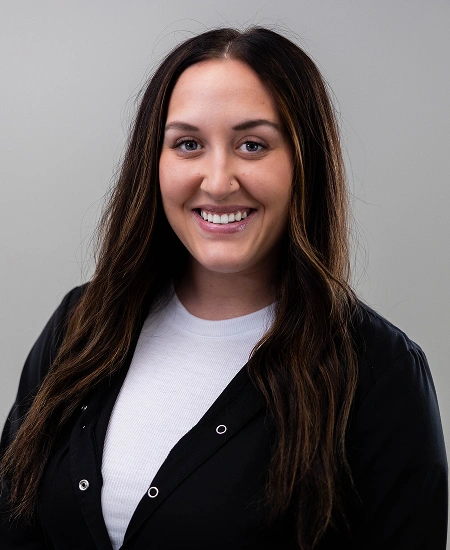 Professional headshot of smiling woman in black cardigan against gray background for orthodontics practice.
