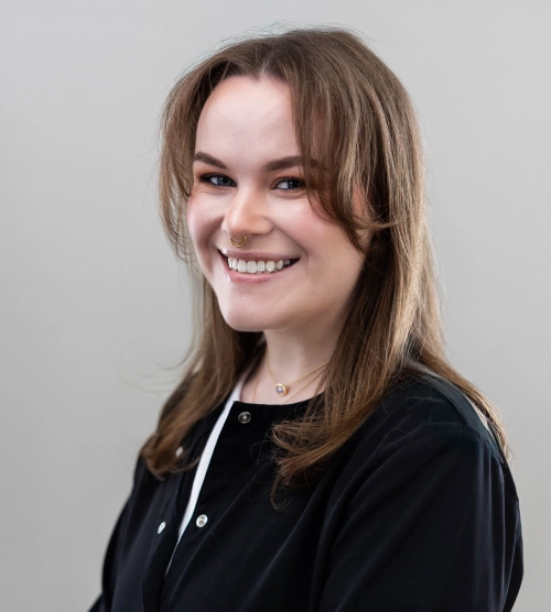Young woman smiling at camera, wearing black jacket, professional headshot against gray background.