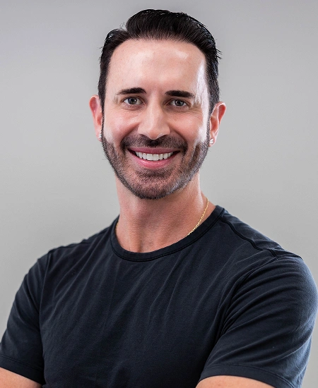 Professional headshot of smiling male team member wearing black t-shirt against neutral gray background.