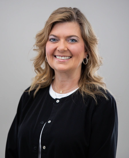 Professional headshot of smiling woman in black cardigan against neutral gray background.