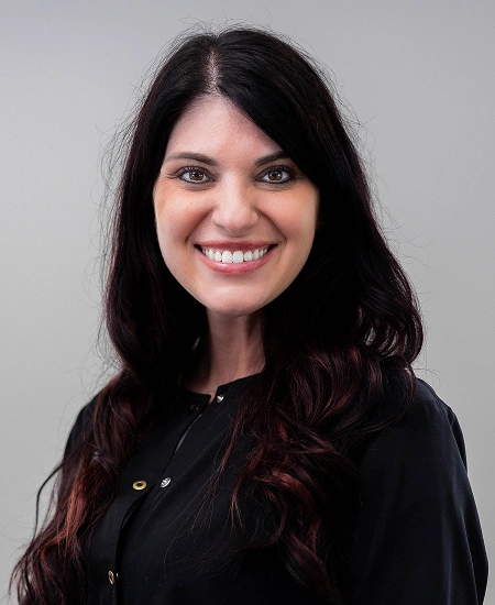 Professional headshot of a smiling woman with long dark hair wearing black against a neutral gray background.