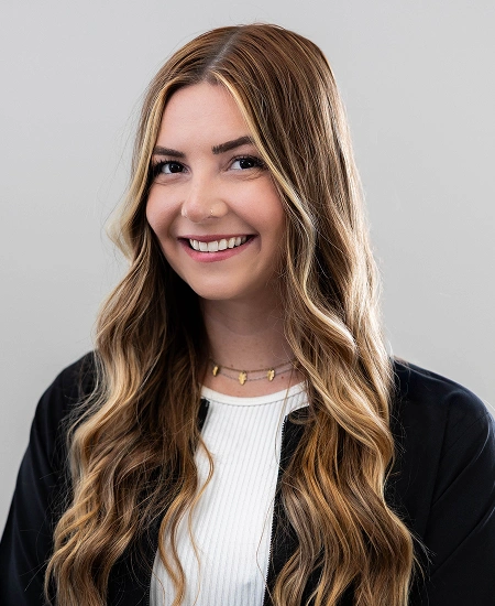 Professional headshot of smiling woman with long brown wavy hair against neutral background.