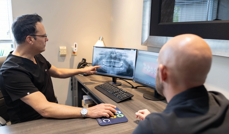 Orthodontist consulting with patient while reviewing dental X-rays on computer monitor in clinical office.