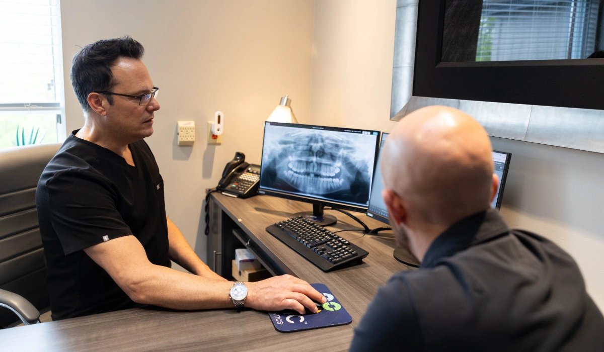 Two orthodontists review digital dental imaging at a desktop computer in a clinical office setting.