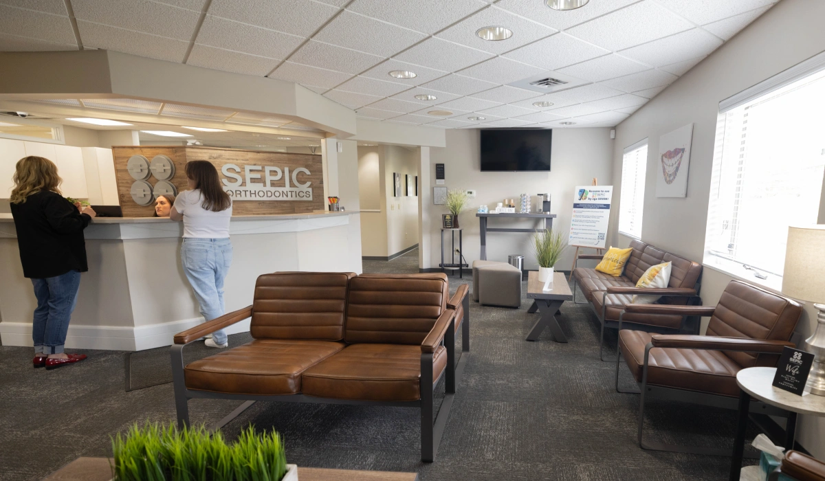 Modern orthodontic office reception area with waiting seating and staff at front desk.