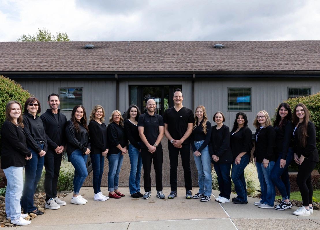Orthodontics team of approximately 20 staff members posing together outside their clinic building.