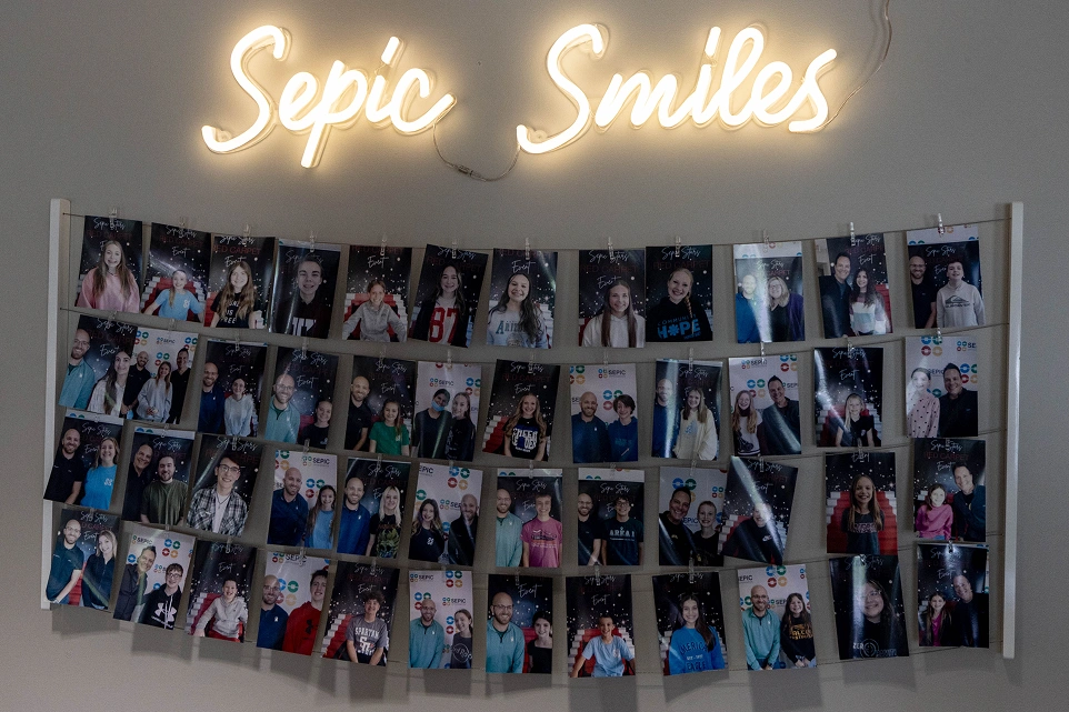 Neon "Sepic Smiles" sign above wall collage of patient photos displaying smiles and memories.
